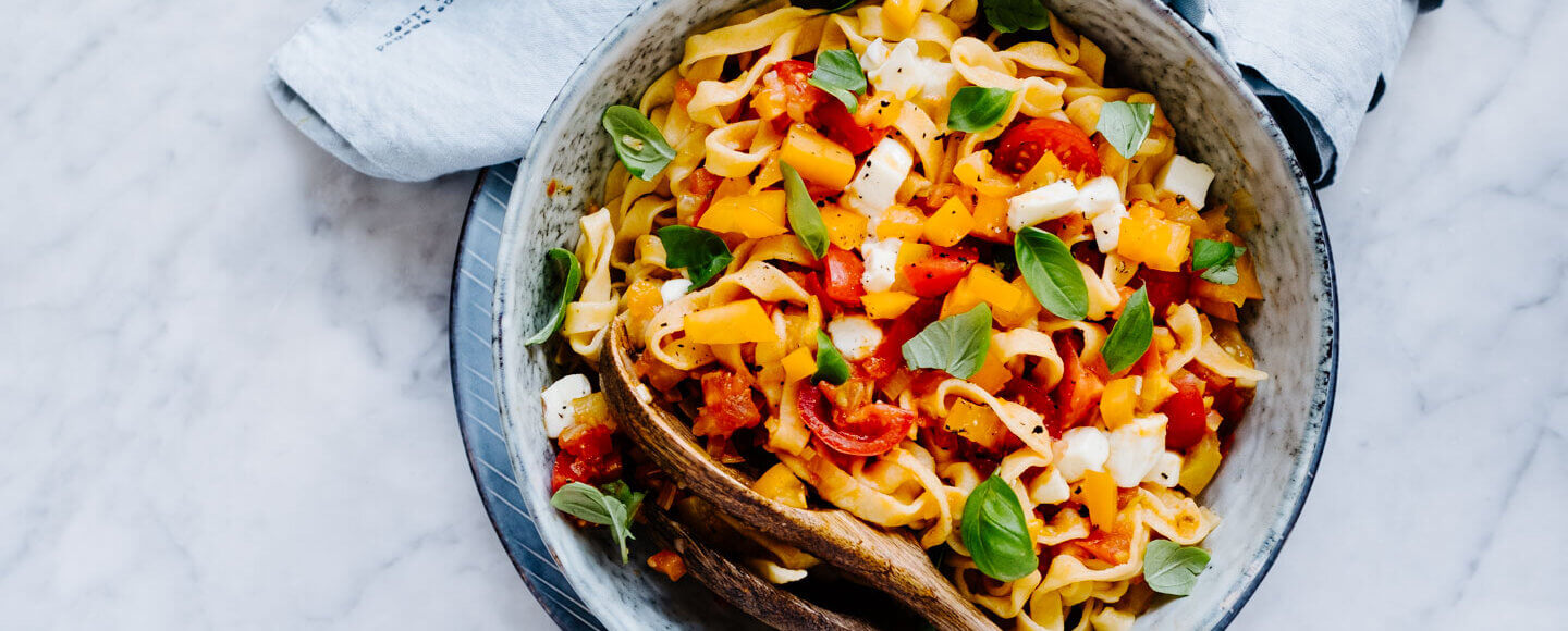 Pasta mit Tomaten-Sugo in Schüssel auf Marmorplatte