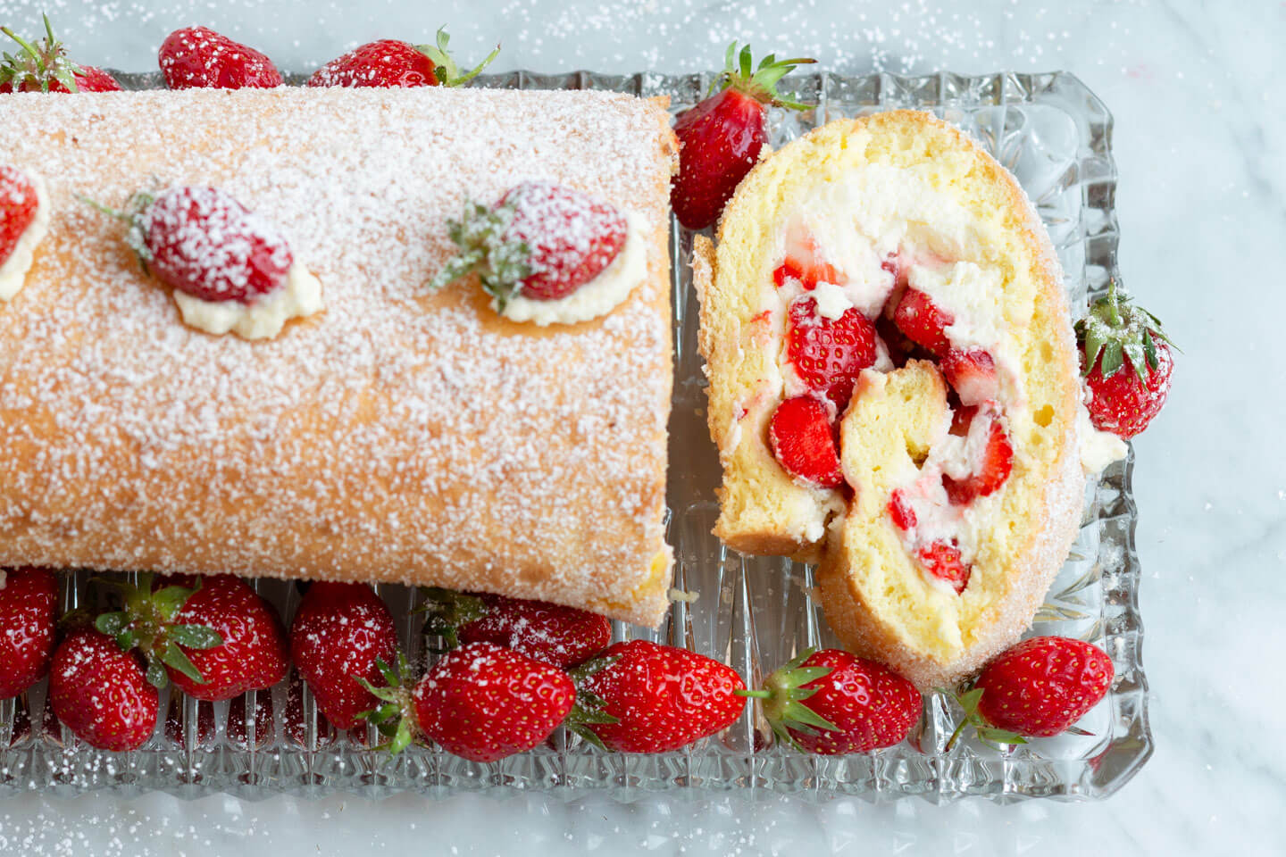 Biskuitrolle mit Sahne und Erdbeeren auf Kuchenplatte